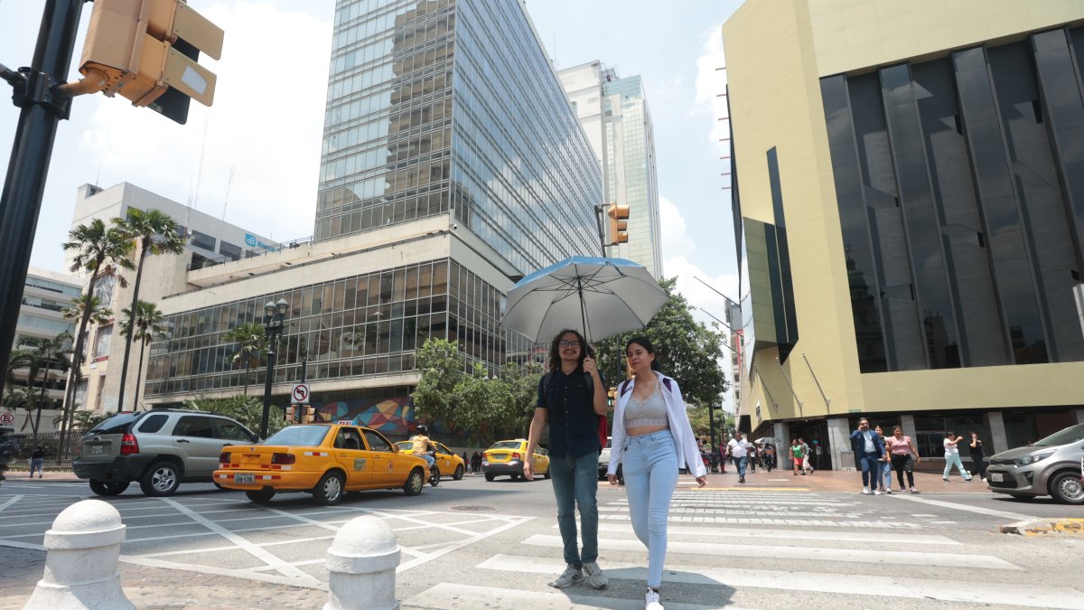 Un para de personas atraviesa una calle de Guayaquil en un día de mucho sol.