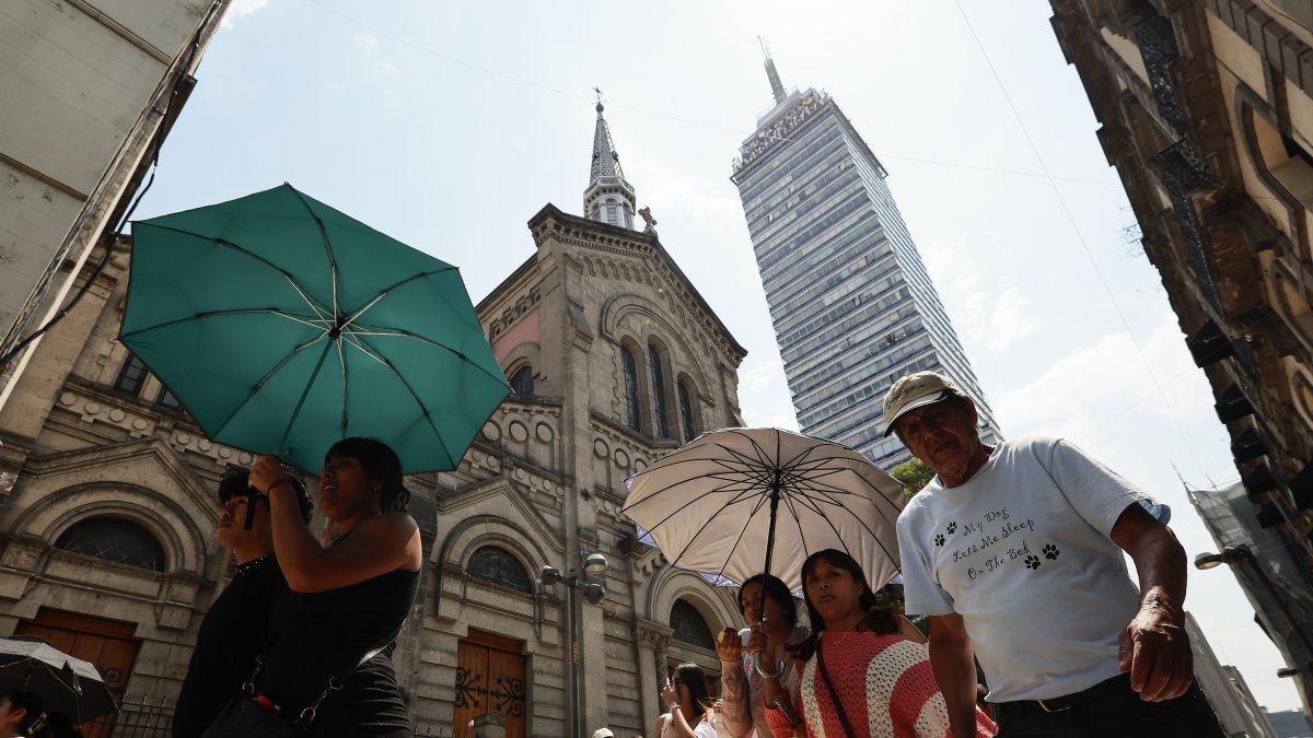 Varias personas caminan con sombrilla para protegerse del sol, este jueves en Ciudad de México (México).
