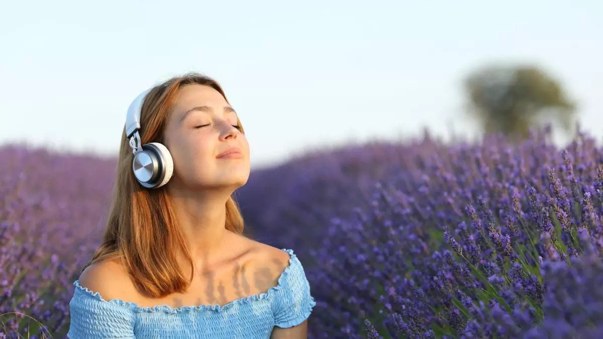 Mujer con auriculares respirando aire fresco en un campo de lavanda.