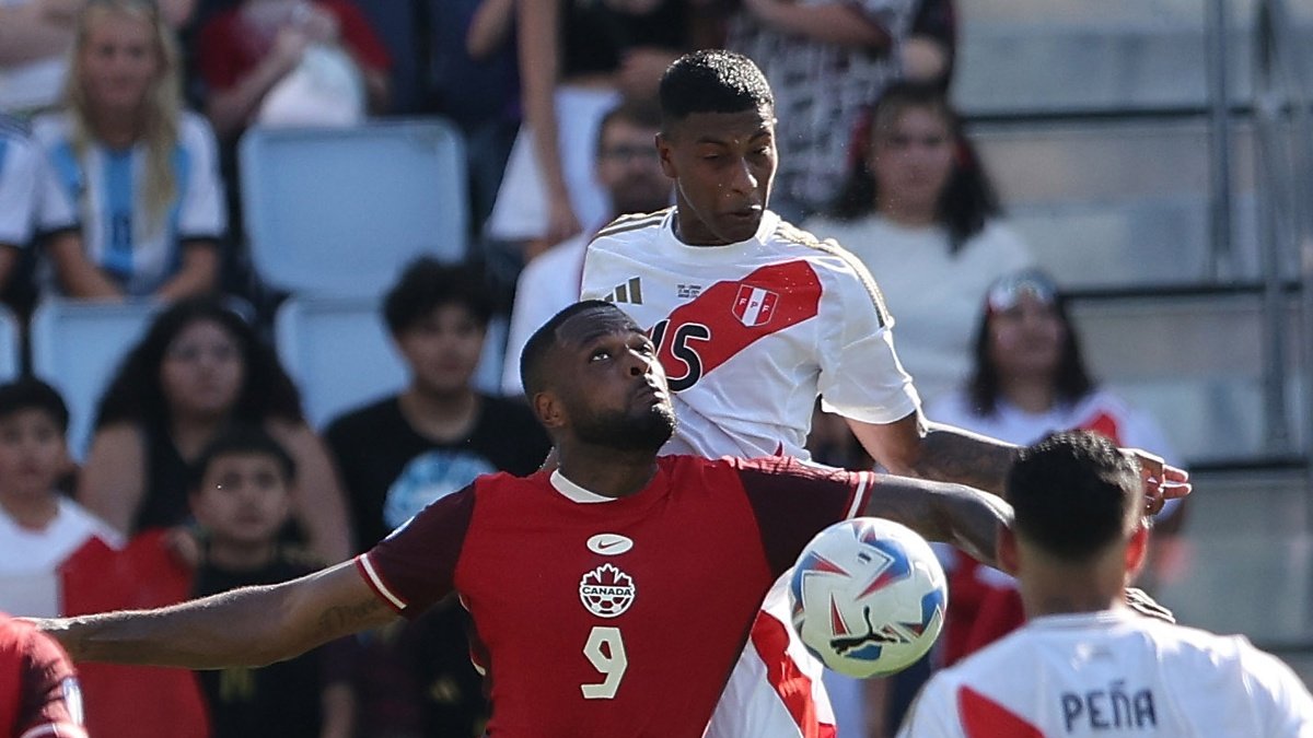 El delantero canadiense Cyle Larin (L) y el defensor peruano Miguel Araujo (R) desafían el balón durante la primera mitad del partido.