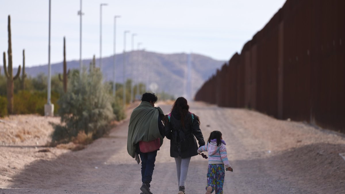 Una familia camina a lo largo del muro fronterizo de Estados Unidos buscando a la Patrulla Fronteriza estadounidense para entregarse para su procesamiento.