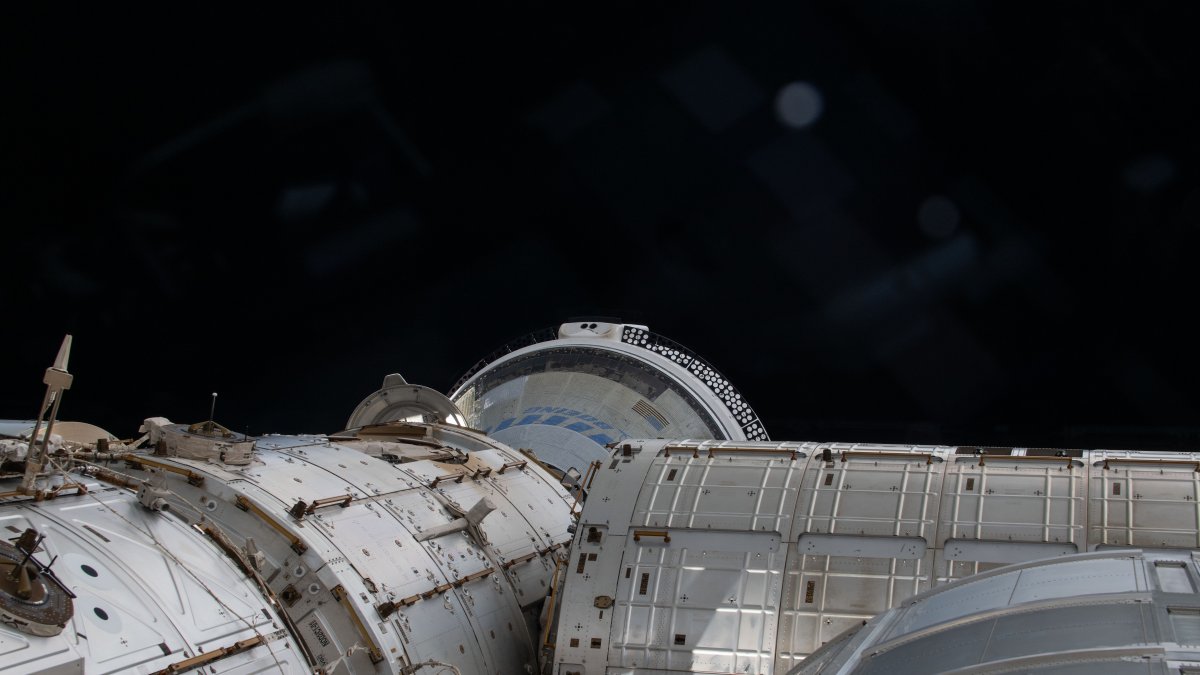 Una instantánea tomada el día 6 de junio de 2024 desde una ventana donde se muestra en una parte el espacio y la nave espacial Starliner de Boeing atracada en la Estación Espacial Internacional (EEI).