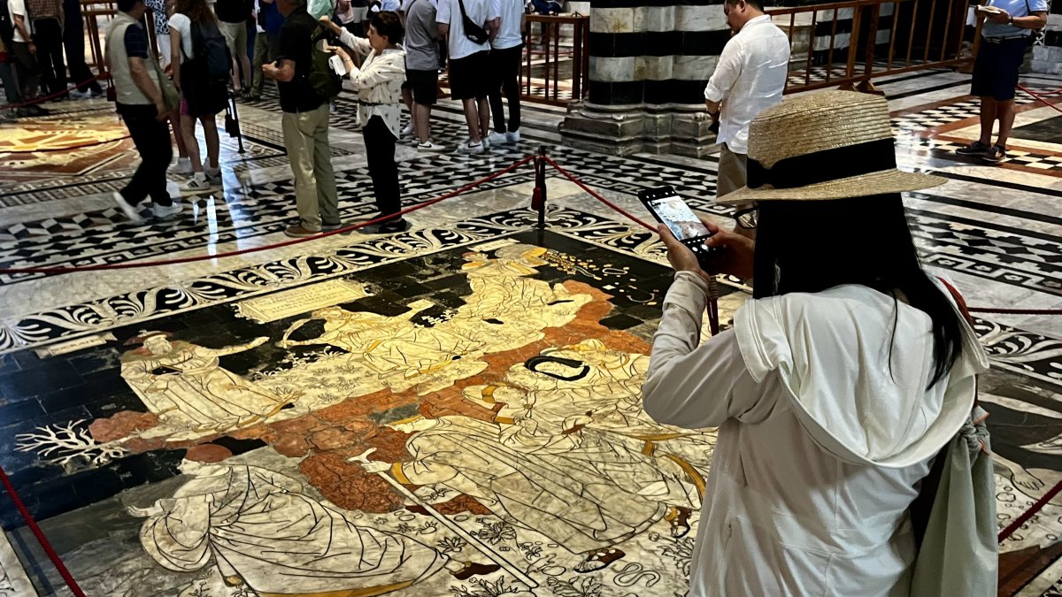 Visitantes de la catedral de la ciudad italiana de Siena observan  las decenas de mosaicos y escenas que decoran el pavimento del templo.