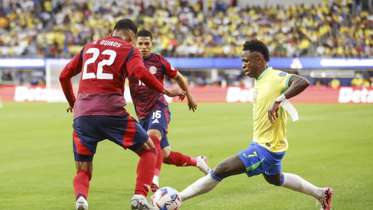 El delantero brasileño Vinicius Junior (d) intenta pasar por el defensor costarricense Haxzel Quiros (i) y el centrocampista costarricense Alejandro Bran (C) durante la segunda mitad de la CONMEBOL.