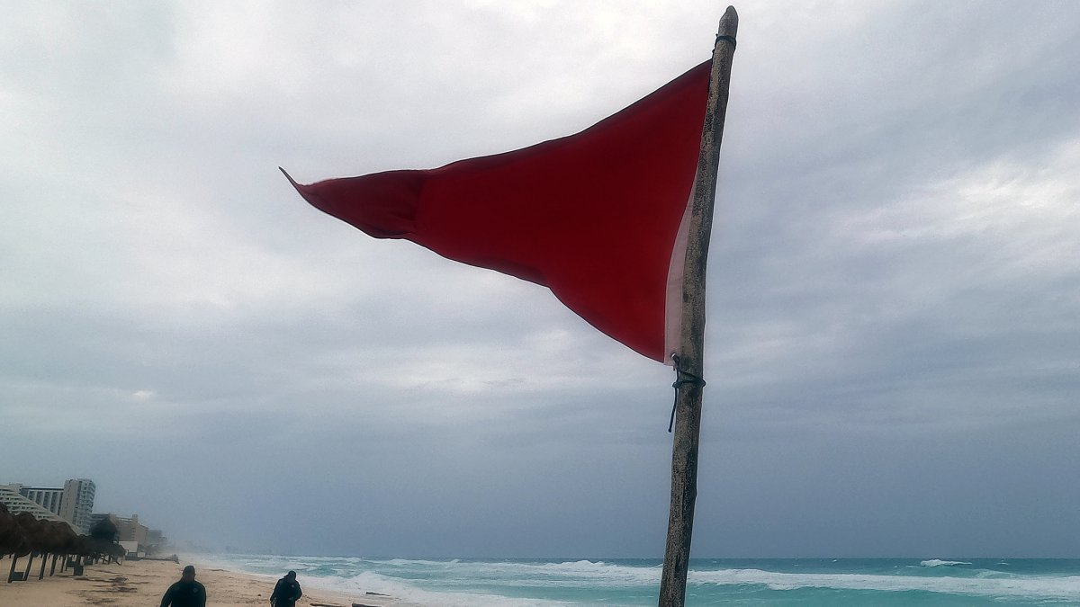 una bandera roja en la playa que indica oleaje agitado y fuertes corrientes debido a la proximidad de la tormenta tropical 'Beryl', en Cancún.
