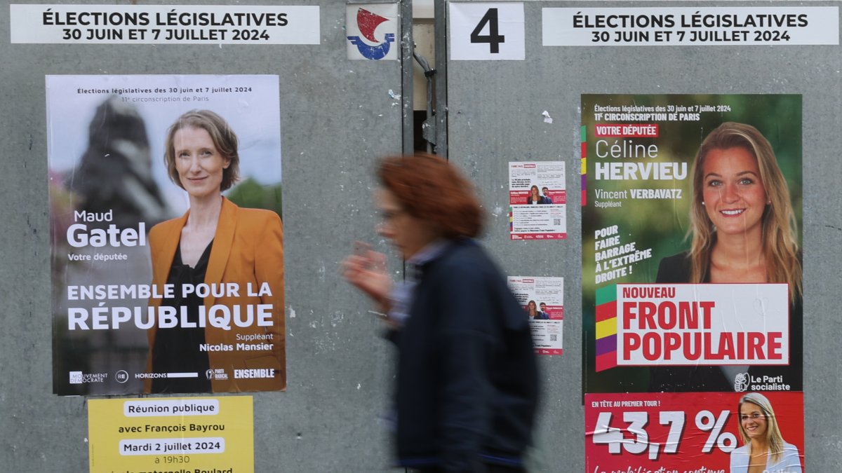 Una mujer pasa por un cartel de los candidatos (R) del Nouveau Front Populaire 'el Nuevo frente Popular' para las elecciones parlamentarias en París, Francia.