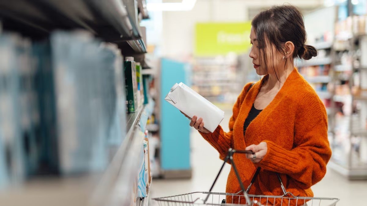 Una joven consulta la información de un cartón de leche en un supermercado.
