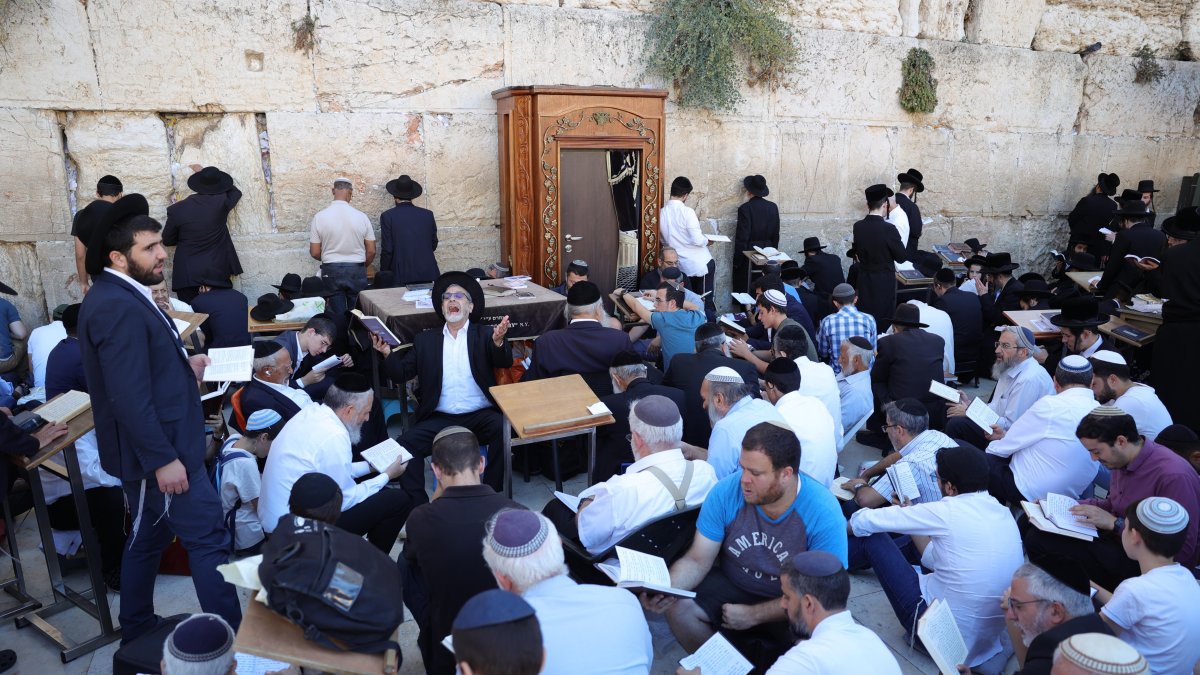 Los judíos ortodoxos rezan mientras leen el libro de Eicha para conmemorar Tishá B'av, en el Muro de las Lamentaciones, en la Ciudad Vieja de Jerusalén, el 13 de agosto de 2024.