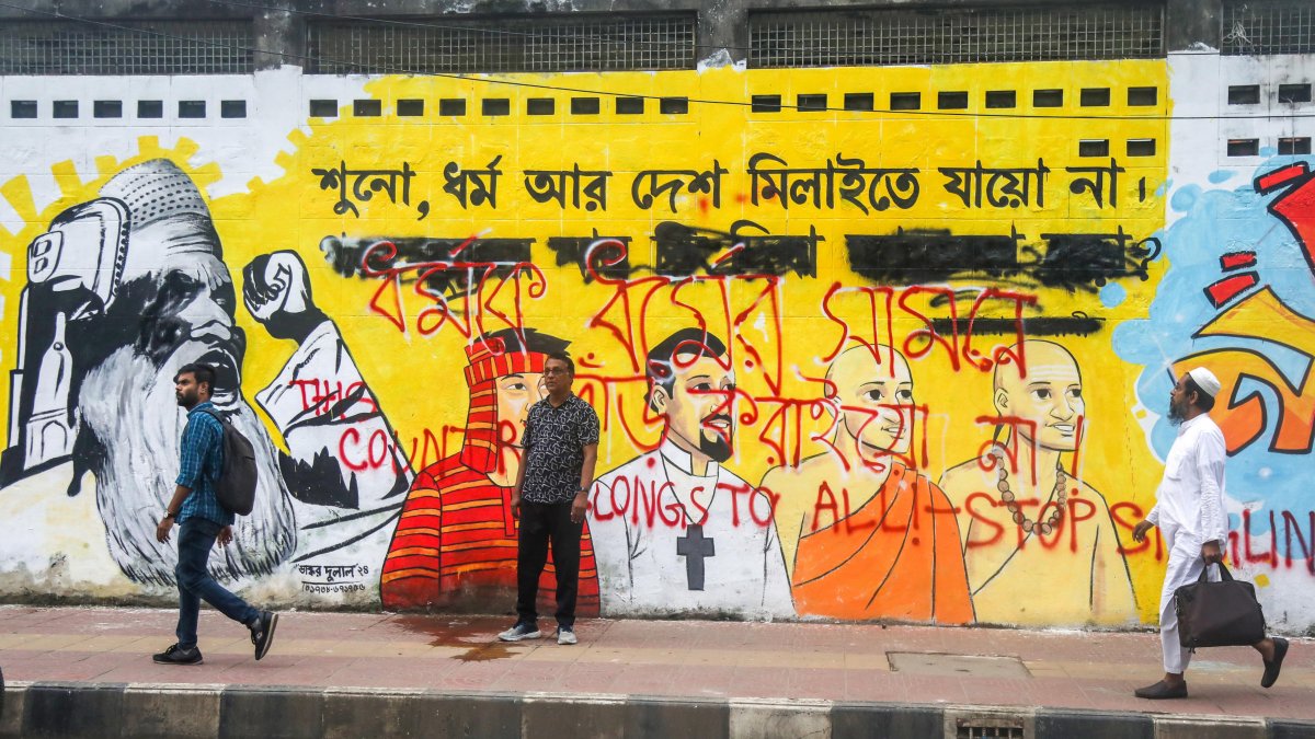 Varias personas caminan junto a un mural en una calle de Daca.