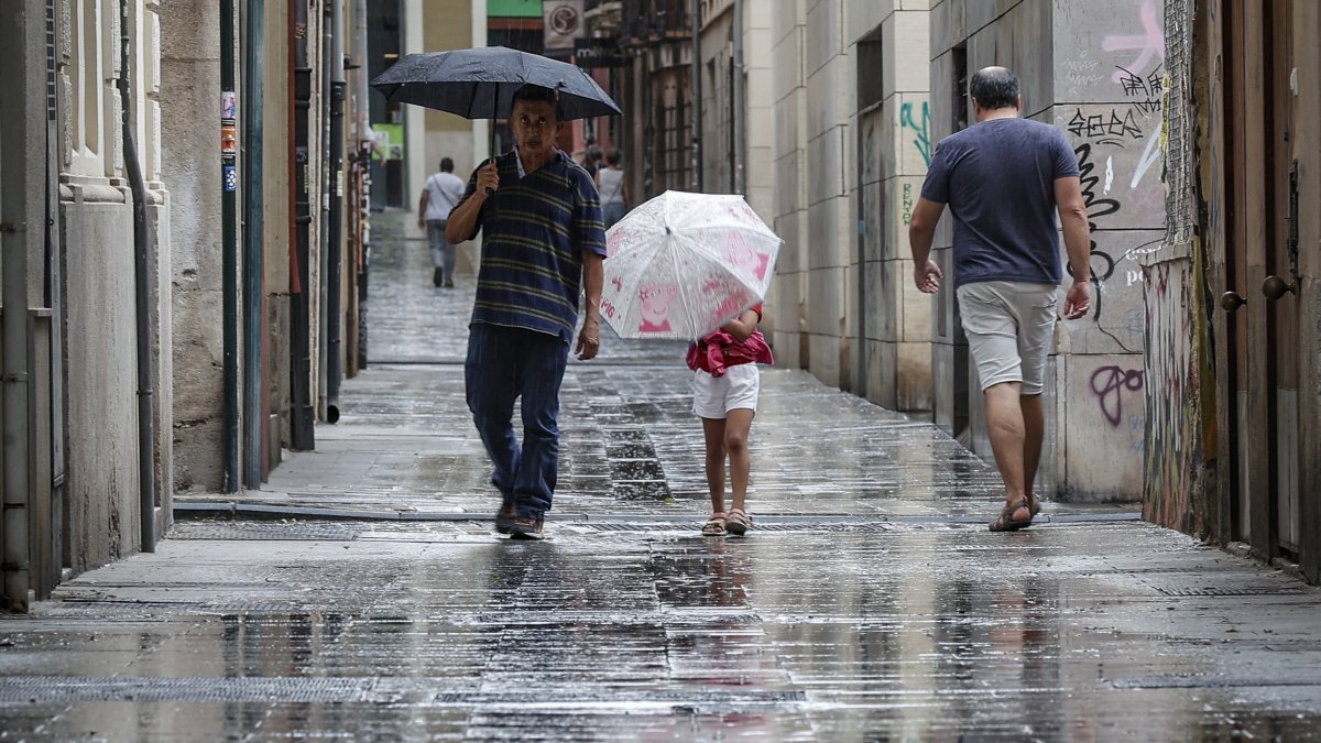 Varias personas caminan bajo la lluvia por una calle del centro de Valencia.