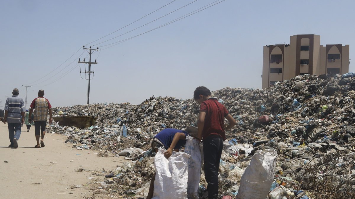 Un  par de niños reciclan de entre una alta y larga montaña de basura que crece y crece según vaya durando el conflicto bélico entre Israel y Hamás. Nadie recoge los desechos en la Franja.