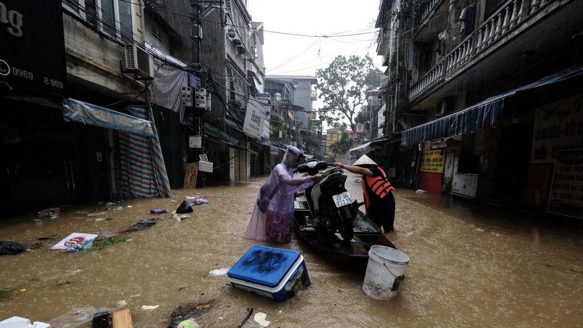 Unas personas en una barca cargada con una motocicleta a través de las aguas inundadas, en Hanoi, Vietnam, este miércoles.