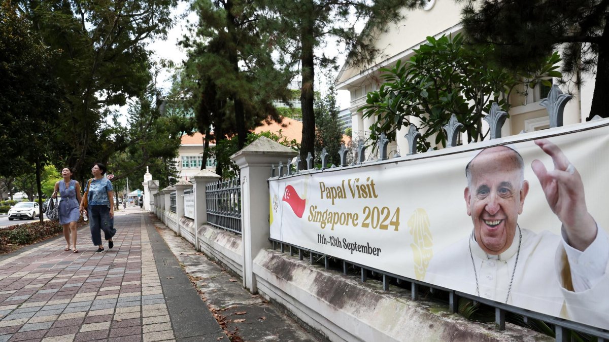 La gente pasa junto a una pancarta que da la bienvenida al Papa Francisco antes de su llegada a Singapur, el 11 de septiembre de 2024.