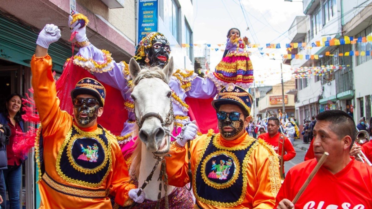 La Mama Negra montada en un caballo, luce vistosos colores y está acompañada por los negros loeros.