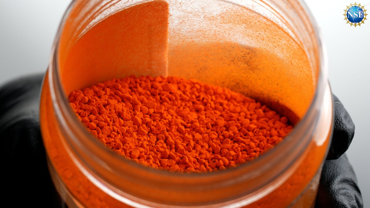 Primer plano de una mano enguantada sacando colorante FD & C Yellow 5 sin disolver de un tarro de cristal. 