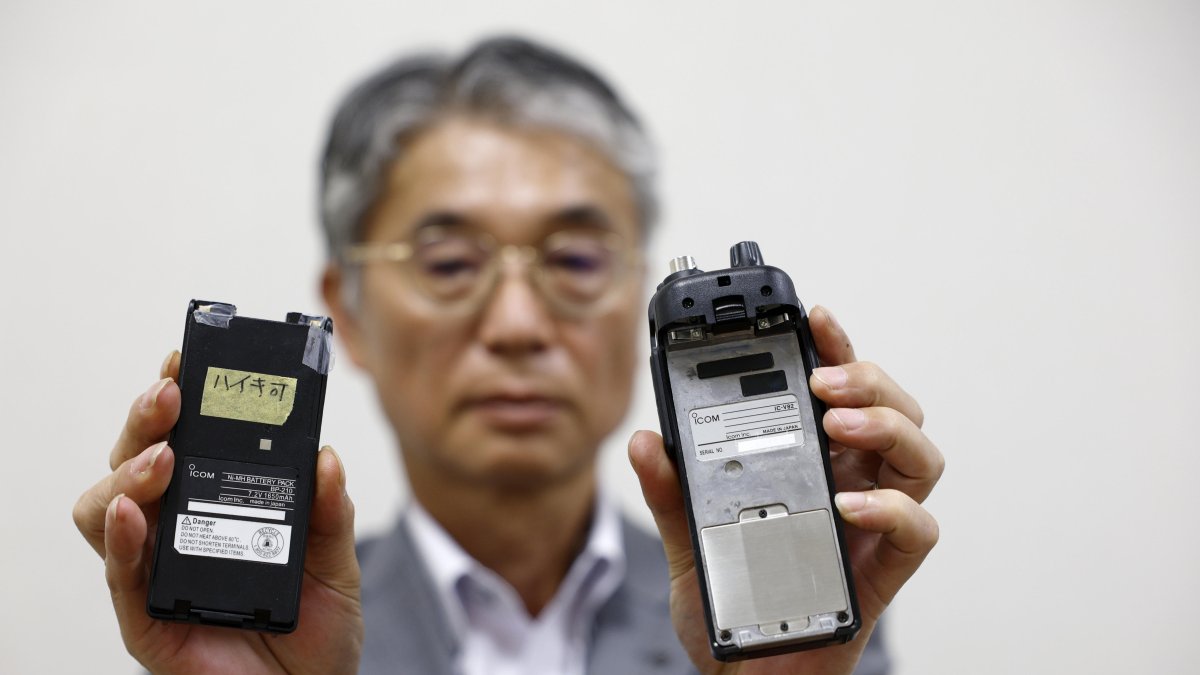 El director del fabricante japonés de walkie-talkie Icom Inc., Yoshiki Enomoto, muestra su dispositivo de radio modelo IC-V82 y su batería (L) en la oficina central de la empresa en Osaka.