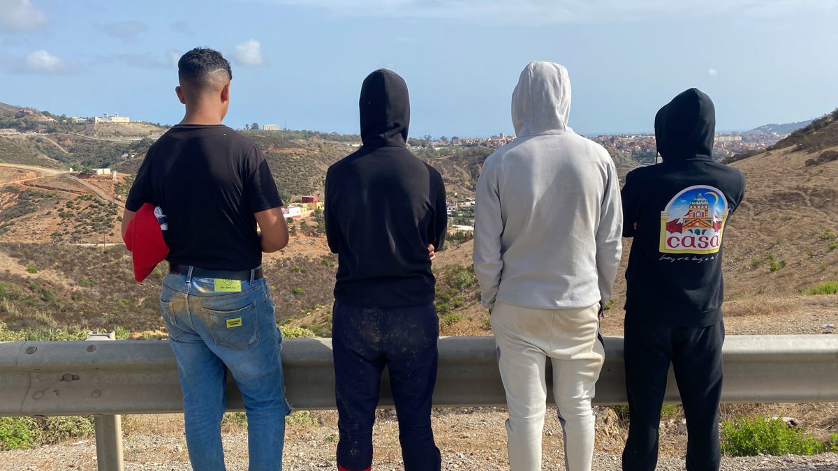 Adam (d) y otros jóvenes miran hacia Ceuta en una carretera a un kilómetro de Fnideq (Castillejos).