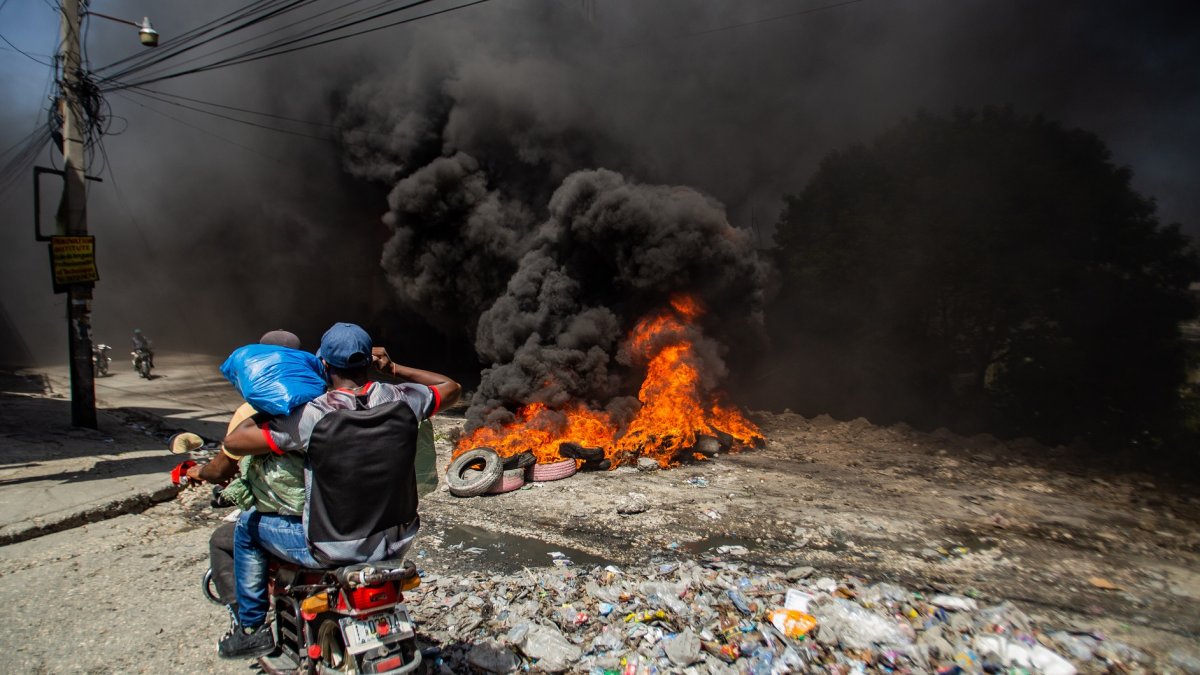 Puerto Príncipe. Dos hombres pasan frente a barricada con fuego.
