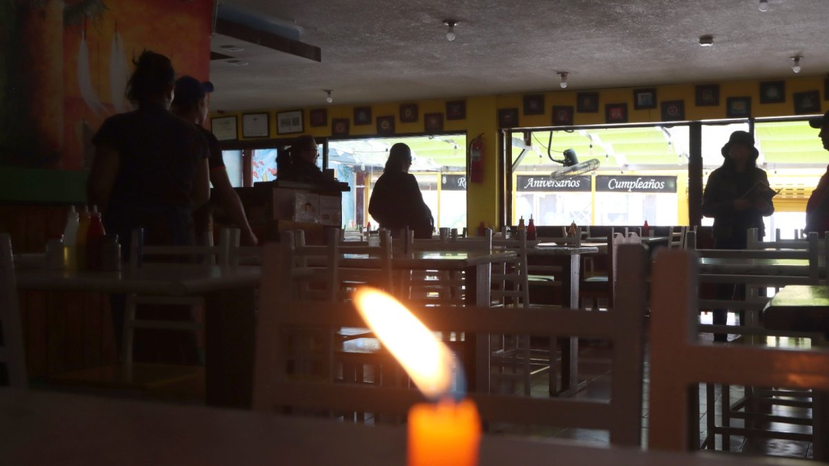 En las mesas de un restaurante se colocaron velas por la falta de luz. La afluencia de clientes disminuyó en comparación con un día normal.