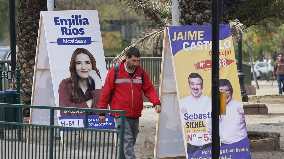 Un hombre camina frente a un afiche con propaganda electoral.