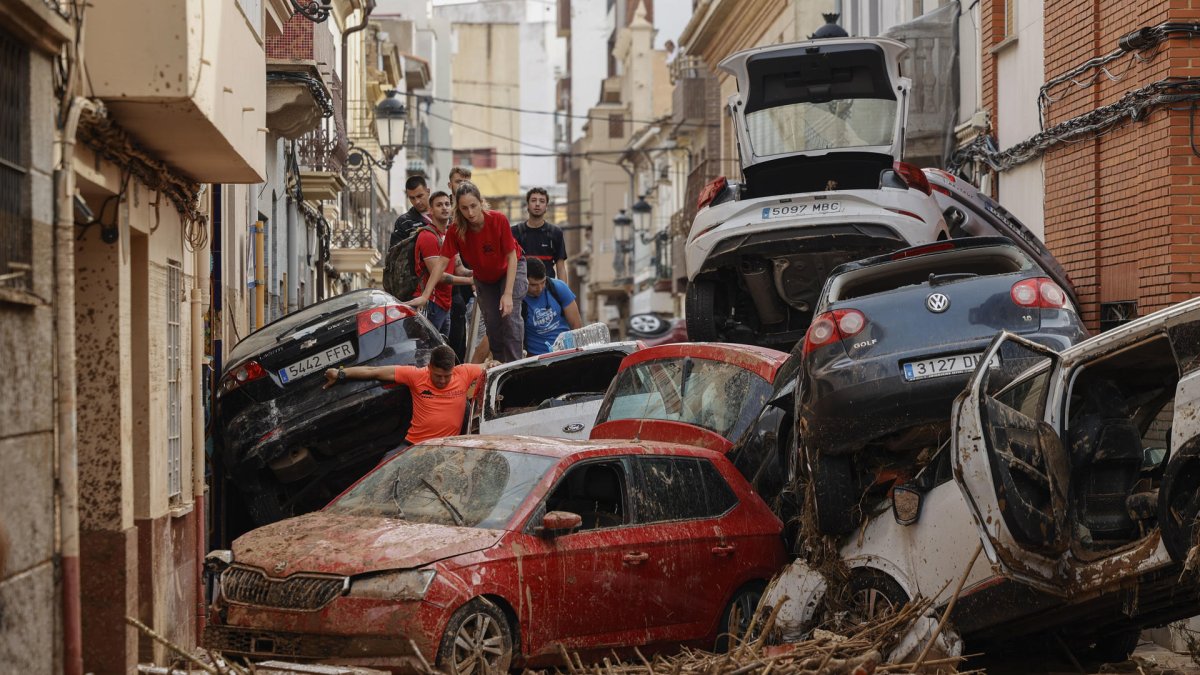 Vecinos de Paiporta intentan pasar entre una montonera de vehículos arrastrados por la corriente, este viernes.
