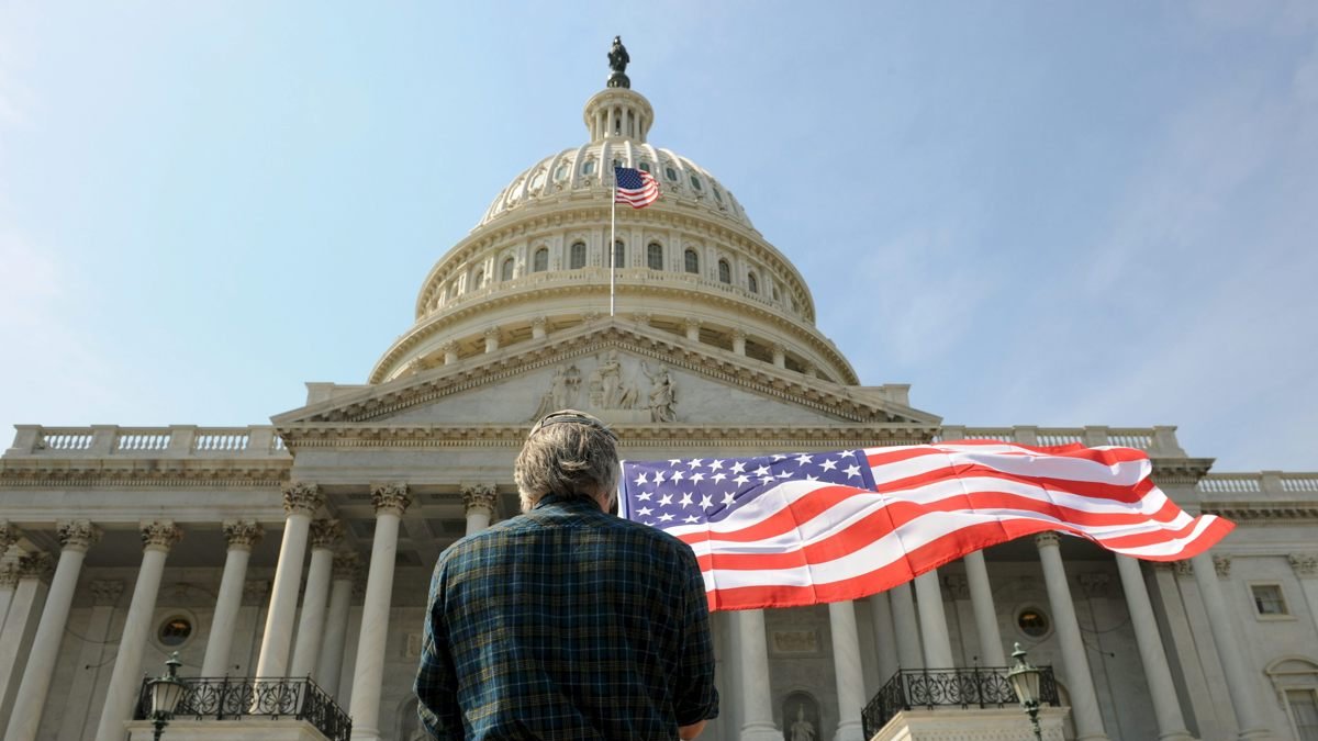 Un hombre con una bandera de los Estados Unidos delante del Capitolio en Washington.