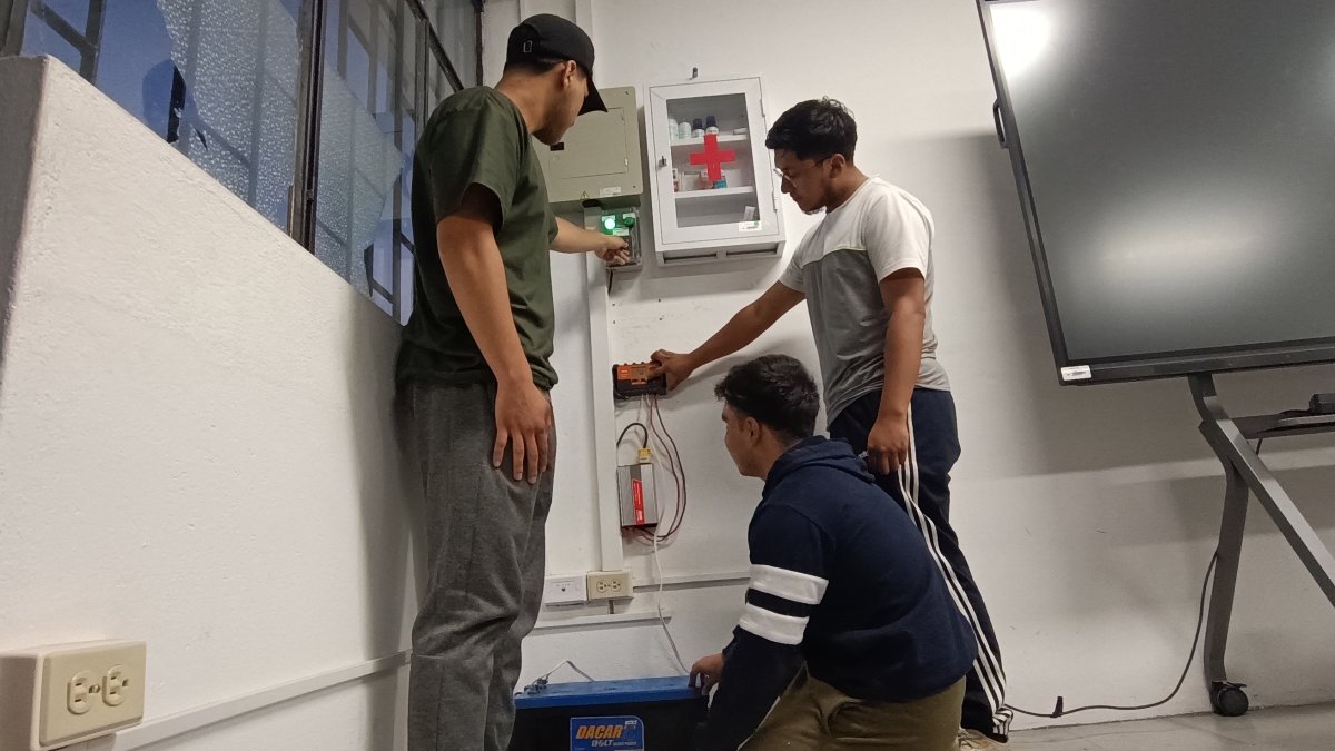 Estudiantes de la Universidad de Cuenca indican las instalaciones eléctricas que permiten transformar la energía de su aula a solar cuando hay cortes de luz./