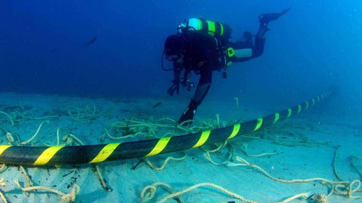 Un buzo se desplaza en las aguas del océano, junto a un cable submarino de fibra óptica.