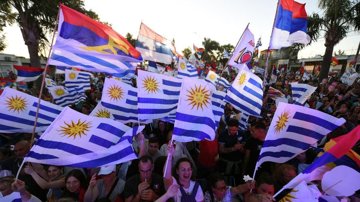 Simpatizantes del candidato por el partido Frente Amplio, Yamandu Orsi, ondean banderas uruguayas y del partido mientras asisten a su mitin de cierre de campaña.