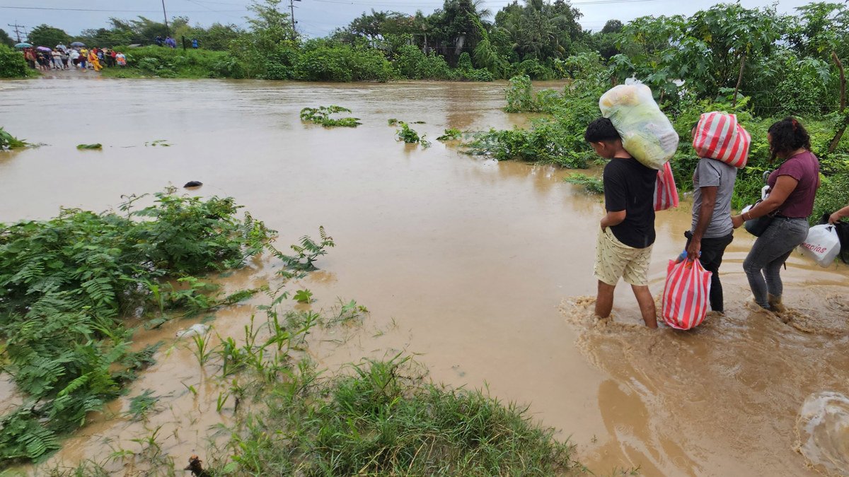 personas cruzan con sus pertenencias por un río en medio de las inundaciones causadas por la tormenta tropical Sara en El Progreso, Honduras.