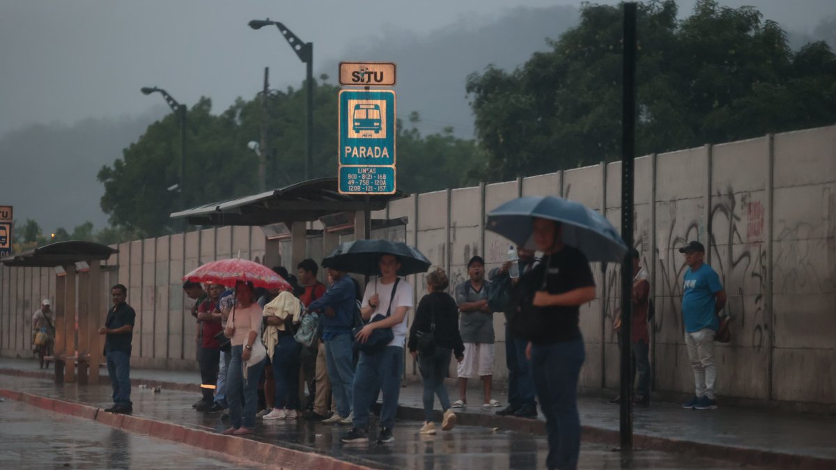 Decenas de usuarios con paraguas permanecen la tarde de este 12 de diciembre a un costado de las vías.