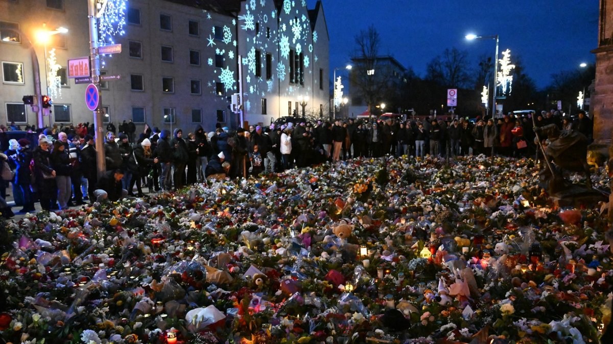 Los dolientes se ubican alrededor de monumento improvisado con flores y velas para las víctimas de un ataque con coche en un mercado navideño en Magdeburgo.