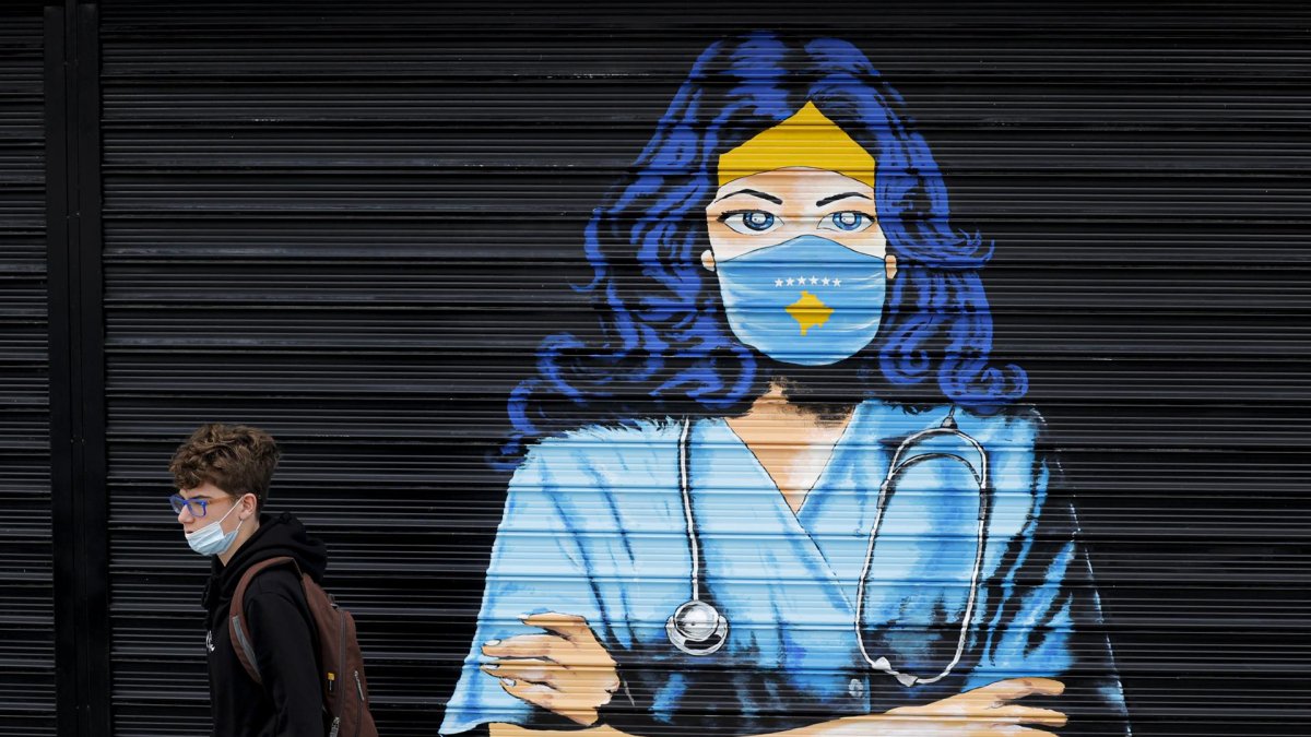 Un chico con mascarilla pasa delante de un mural en Pristina (Kosovo)