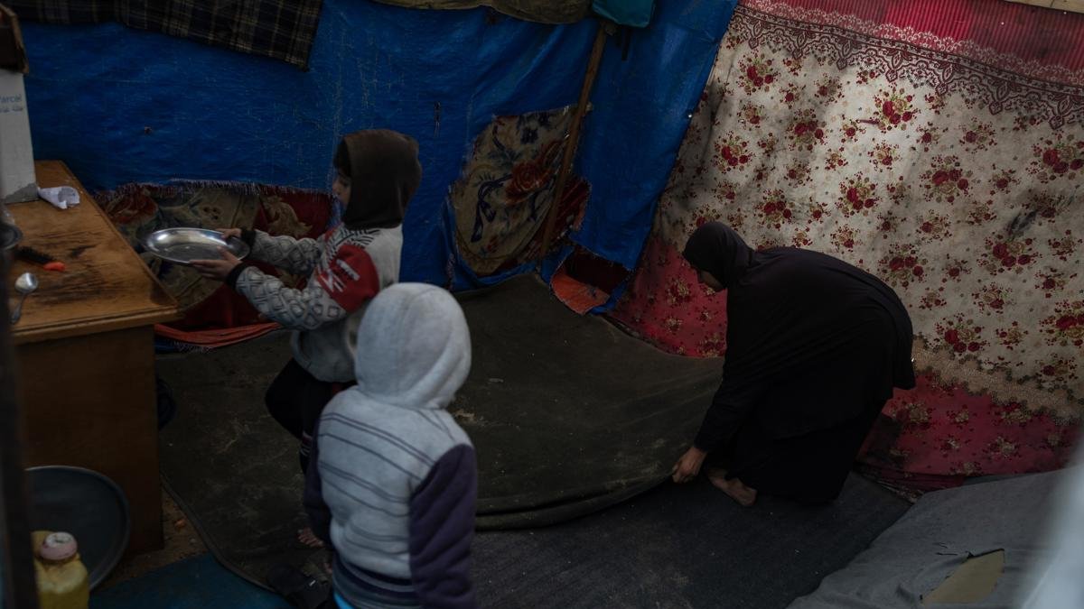 Una mujer palestina desplazada internamente limpia su tienda con sus hijos.
