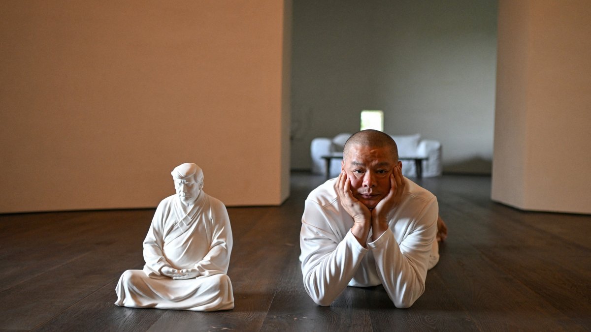 El artista Hong Jinshi posa junto a una escultura del presidente electo Donald Trump, en una pose que evoca a Buda en su taller en Xiamen.