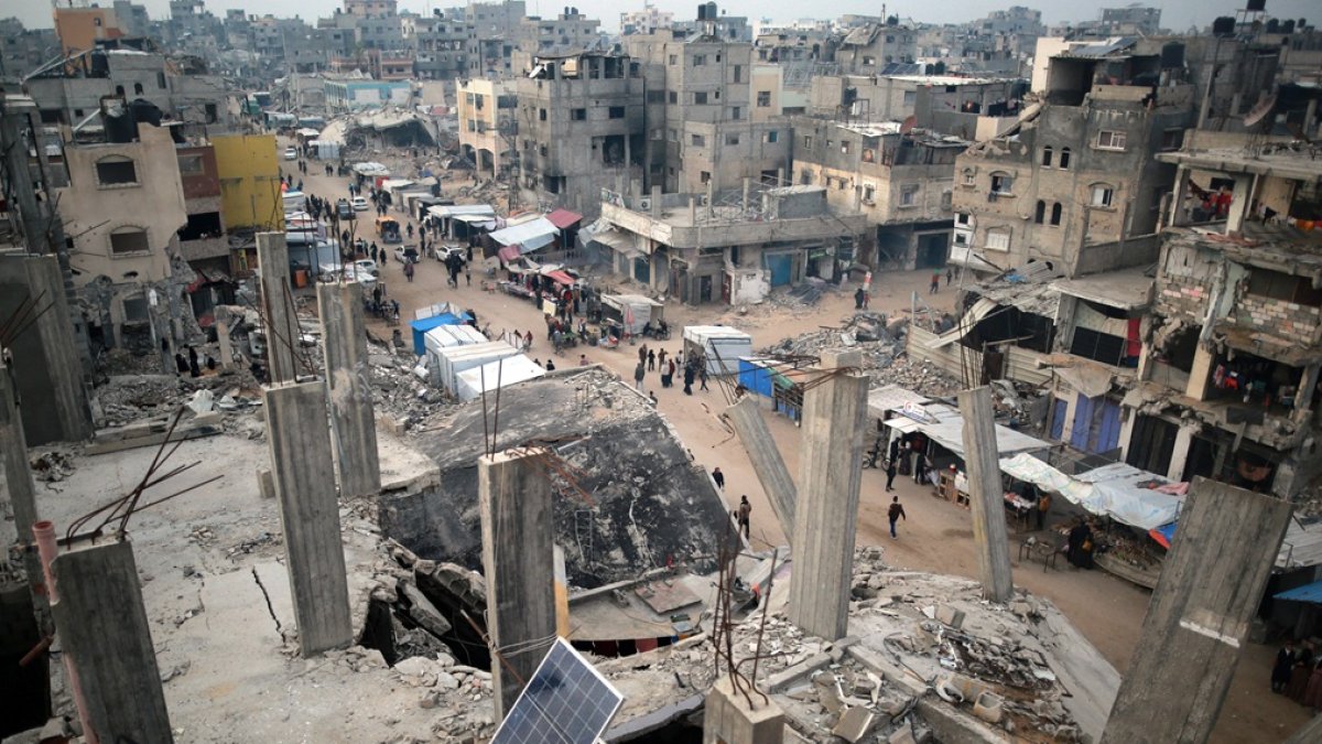 La gente pasa por puestos de venta de productos entre los escombros de los edificios destruidos durante ataques israelíes anteriores, en Khan Yunis.