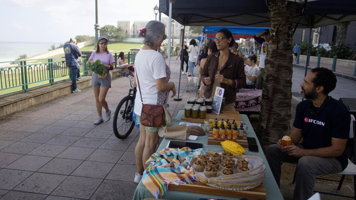 Melissa Scarcliff (c) habla con una clienta junto a José Crespo, en el Mercado Agrícola del Viejo San Juan (Puerto Rico).