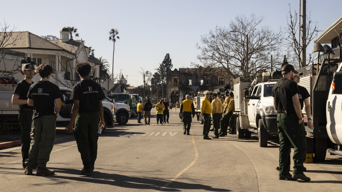 Un edificio carbonizado se ve a lo lejos mientras los empleados de una compañía privada de extinción de incendios, trabajan.