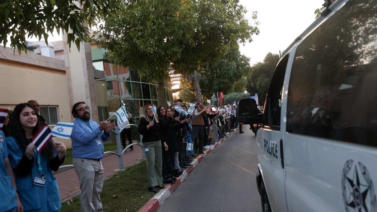 Personas y personal del Centro Médico Shamir frente al complejo hospitalario de Beer Yaakov, ondean banderas mientras llegan ambulancias de la policía que transportan a cinco rehenes recién liberados.