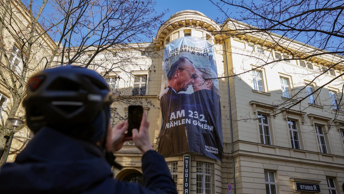 Un hombre toma una foto del cartel que muestra el inicio de un beso entre el favorito de las encuestas, Friedrich Merz, y la candidata ultraderechista Alice Weidel, en Berlín.