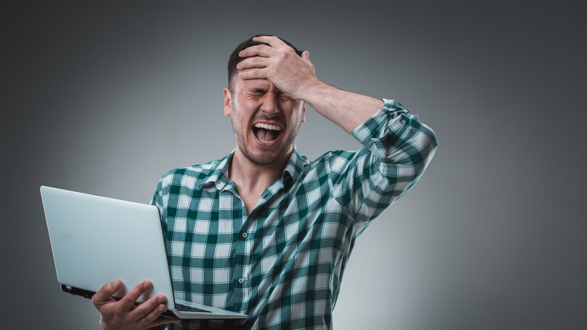 Portrait of young handsome man using laptop, wearing plaid shirt. Studio shot. Emotions