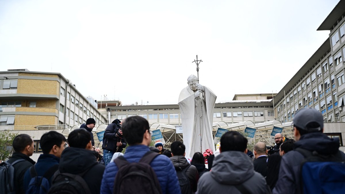 Un grupo de la comunidad vietnamita de Roma reza ante la estatua de Juan Pablo II afuera del hospital Gemelli, donde está hospitalizado el Papa.