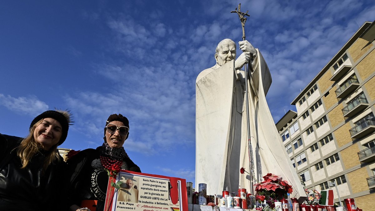Fieles con un cartel frente a la estatua del Papa Juan Pablo II en la entrada del Hospital Gemelli, donde está hospitalizado el Papa Francisco.