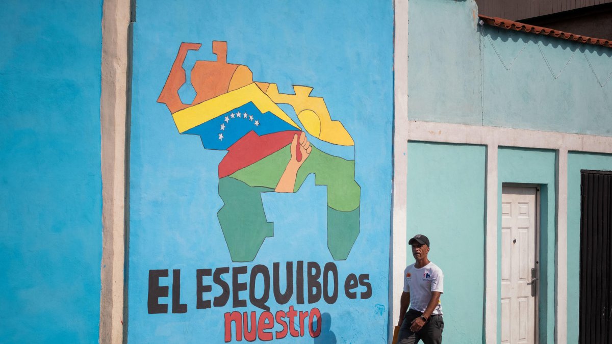 Transeúntes caminando frente a un mural con el mapa de Venezuela que dice 'El Esequibo es nuestro', en Caracas.