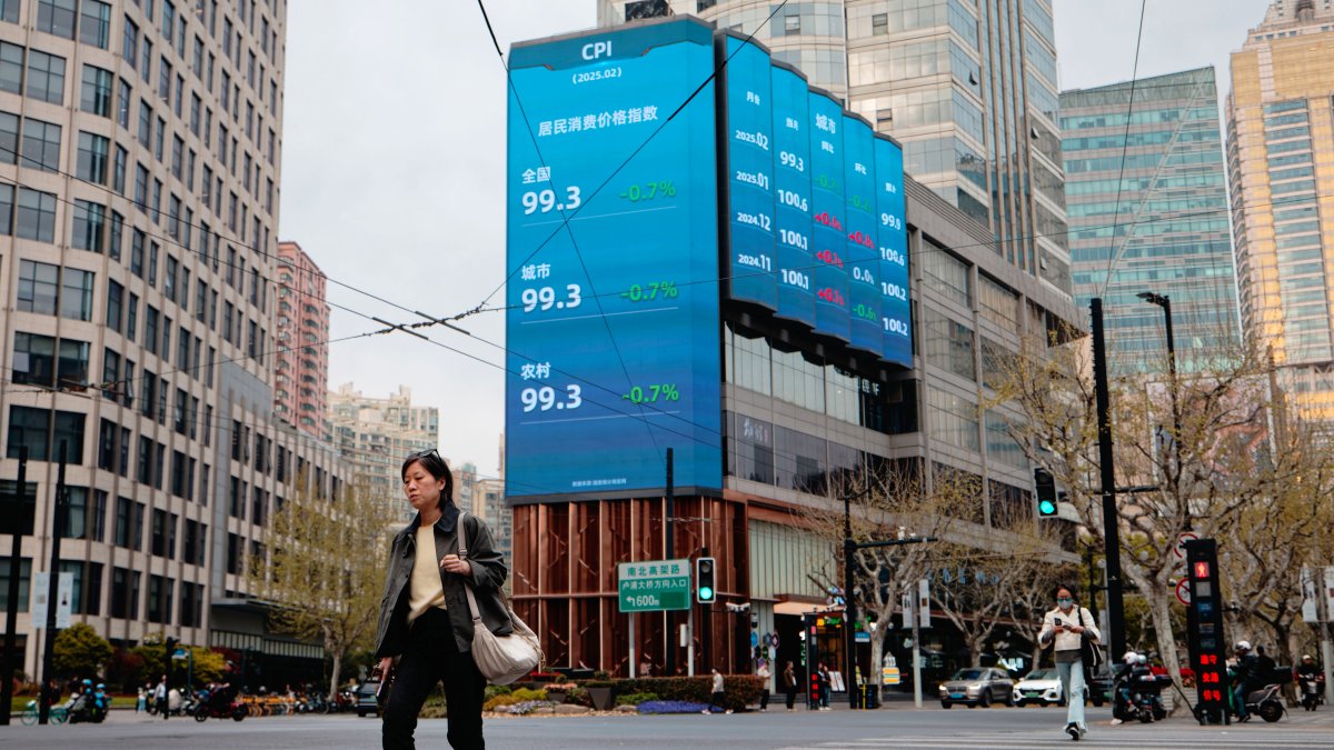 Dos personas caminan por una calle cerca de las pantallas que muestran las cifras de la bolsa de valores en China.