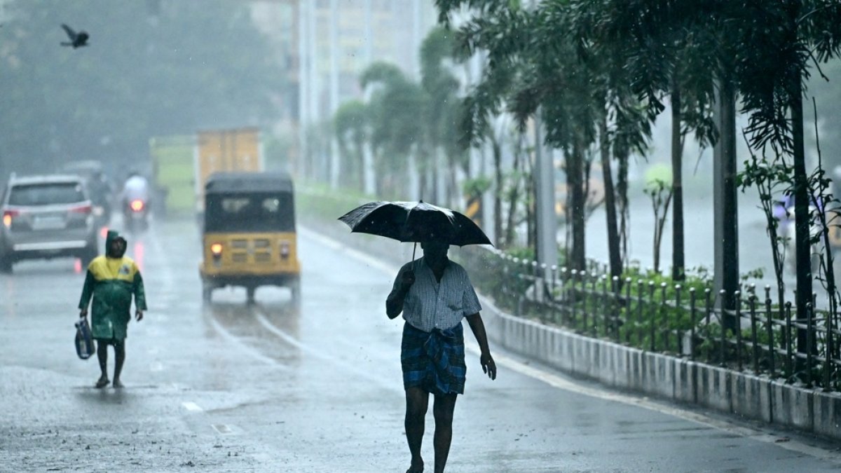 Un hombre que sostiene un paraguas viaja por una calle mientras llueve en Chenna.