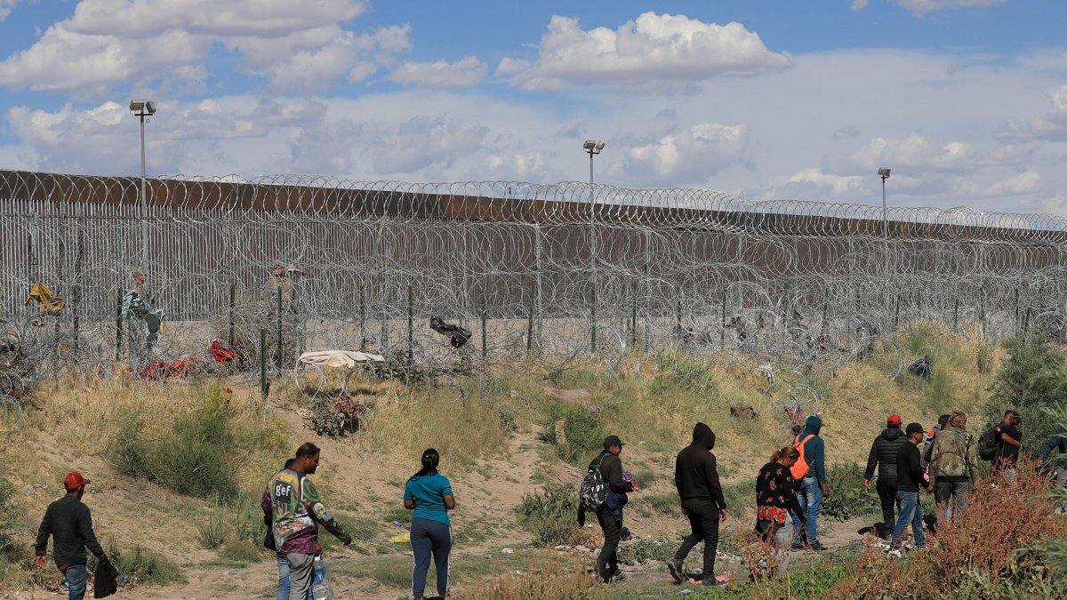 Migrantes caminan cerca del muro que separa la frontera estadounidense en Ciudad Juárez, Chihuahua (México).
