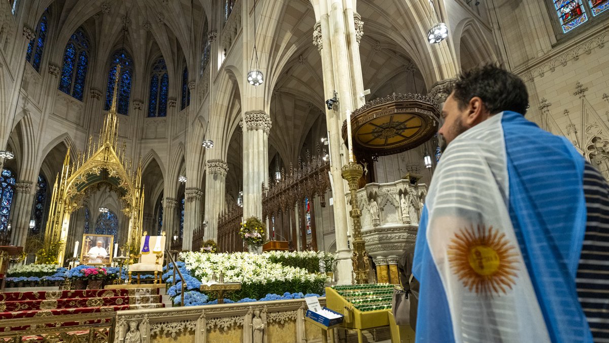 Una persona que lleva la bandera de Argentina mira una imagen del fallecido Papa Francisco dentro de la Catedral de San Patricio.