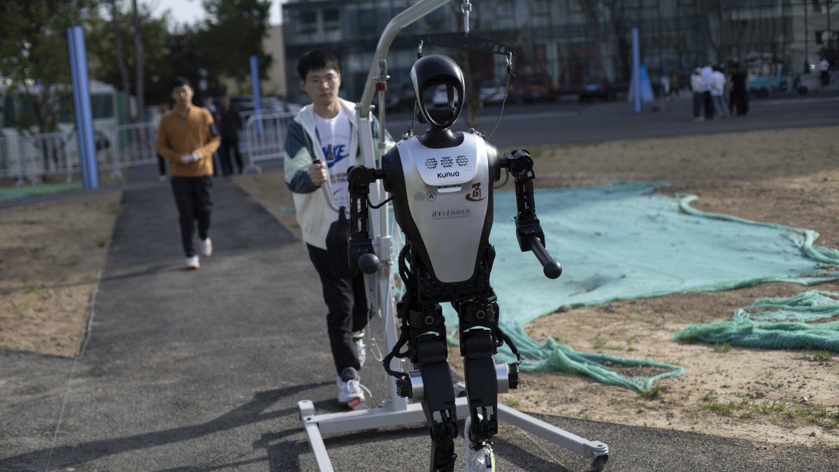 Un técnico camina detrás de un robot humanoide antes de la carrera de humanos y robots en Pekín.
