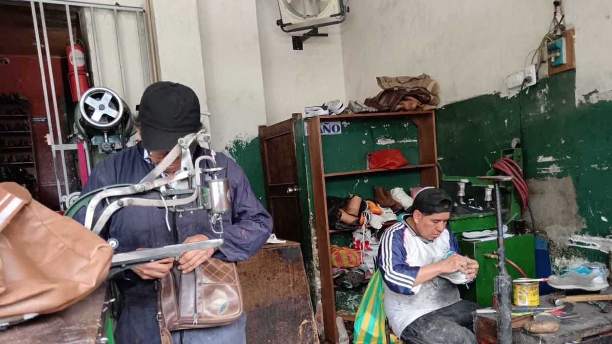 Oswaldo Cujilema (de pie) cose la planta de una zapatilla en su local 'Cosedora Los Andes', donde continúa el legado de su abuelo zapatero.